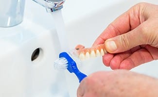 Person cleaning their denture with a toothbrush.