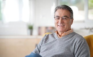 Older man with glasses and grey shirt smiling