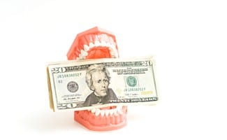Dentures propped open holding twenty-dollar bills