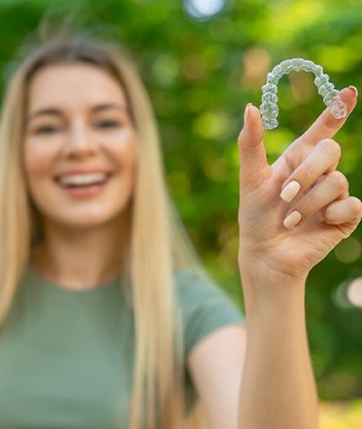 Teenage girl smiling while holding clear aligner