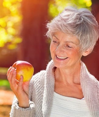 Woman with dental implants in Ocala smiling at an apple