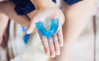 Outstretched hand holding mouthguard to protect dental implants in Ocala