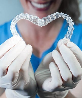 dental hygienist holding two Invisalign trays in the shape of a heart 