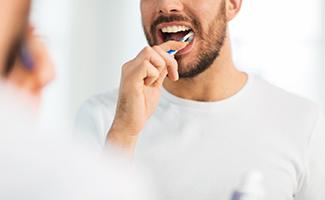 Man in white shirt smiling while brushing his teeth