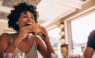 Woman smiling while eating sandwich at restaurant