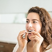 Young woman with brown hair putting clear aligner in mouth