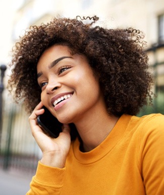 Woman in yellow shirt smiling while talking on phone outside