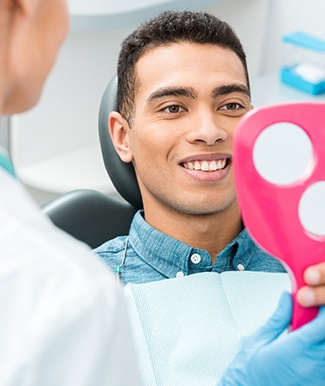 Man smiling at reflection in handheld mirror