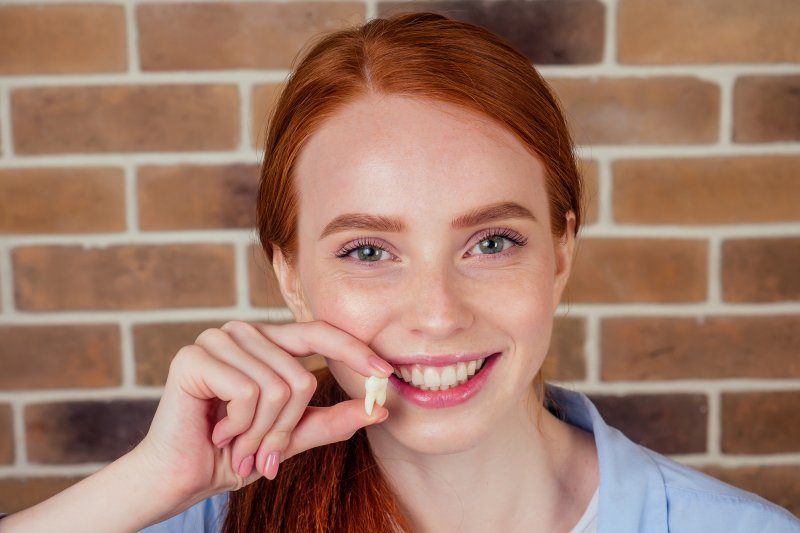 Woman smiling and holding extracted tooth