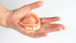 closeup of an older womans hand holding dentures