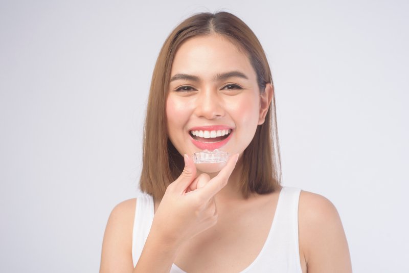 young woman smiling while holding Invisalign clear aligner