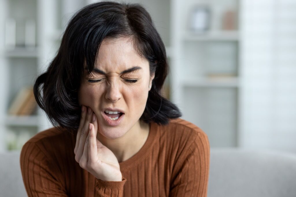 Woman with dark hair squinting in pain pressing hand to jaw